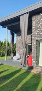 Tamsiai pilkos spalvos terasos užuolaidos, aukštoje klinkerio terasoje, raudonas sėdmaišis terasoje.